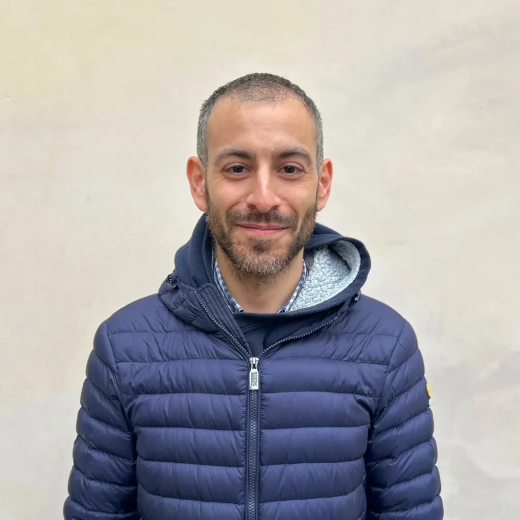 Ritratto di uno studente di 42 Firenze sorridente, con un piumino blu, su sfondo chiaro.